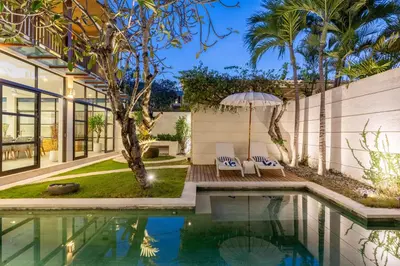 a pool in the backyard of a house with two chairs and an umbrella at Villa Lumut 3 Bedrooms Central Seminyak in Seminyak
