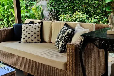 a wicker couch with pillows on a patio at Miracle Villa Sanur in Sanur