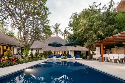 a swimming pool in front of a house with chairs and umbrellas at The Indies Estate in Sanur