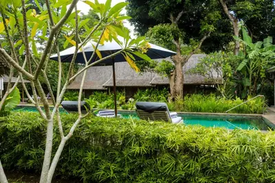 a swimming pool with two chairs and an umbrella at Chanteak Bali - Stone House 2 in Jimbaran