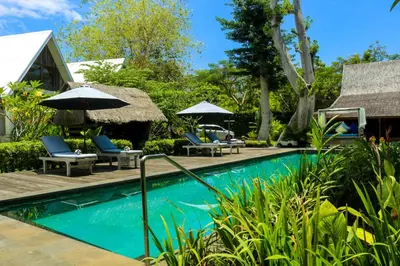 a pool at a resort with chairs and umbrellas at Chanteak Bali - Teak House 1 in Jimbaran