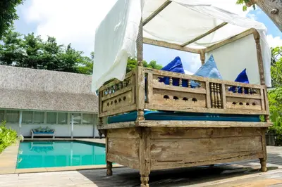a wooden bed in front of a swimming pool at Chanteak Bali - Teak House 2 in Jimbaran