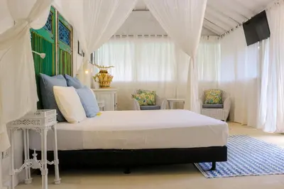 a bedroom with a bed with curtains and a television at Chanteak Bali - White House 1 in Jimbaran