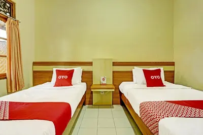 two beds with red pillows in a room at OYO Collection O 91125 Puri Dewa Bharata in Jimbaran