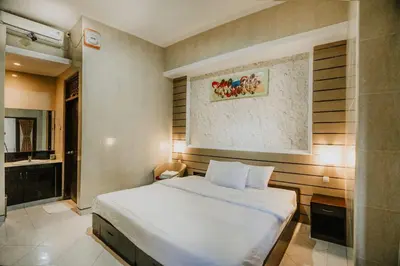 a bedroom with a white bed and a bathroom at DENAYS GUESTHOUSE JIMBARAN in Jimbaran