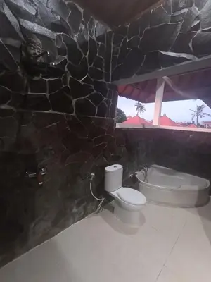 a bathroom with a toilet and a stone wall at Kusnadi Hotel in Legian
