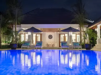 a swimming pool at night with chairs and umbrellas at Villa Windu Asri in Seminyak