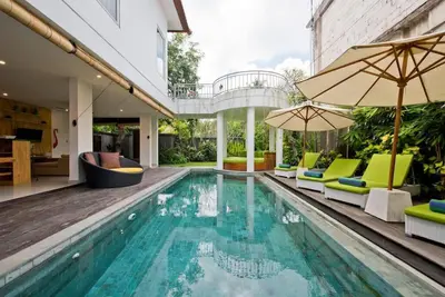 a pool with chairs and umbrellas next to a house at 3BR Del Mar Beach Villas Near La Plancha Seminyak in Seminyak