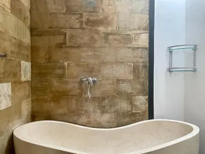 a bath tub in a bathroom with a stone wall at VILLA LUNA in Kerobokan