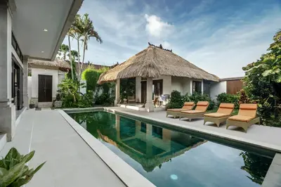 a house with a swimming pool with chairs and a thatch roof at Villa Gading by Alfred in Bali in Seminyak
