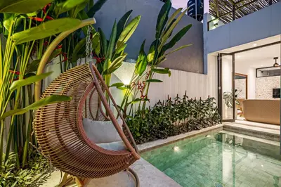a swinging rattan chair next to a swimming pool at Besso Villa by Betterplace in Canggu