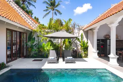a house with a swimming pool and two chairs and an umbrella at Villa Rua - Stylish luxury, tranquil location in Legian, walk to beach in Seminyak