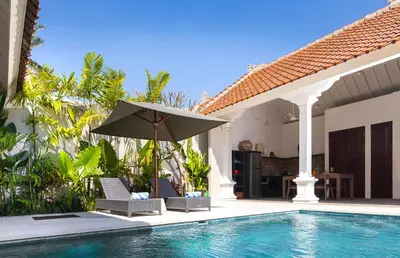 a pool with chairs and an umbrella next to a house at Villa Tahi - Stylish luxury, tranquil location, walk to beach in Legian