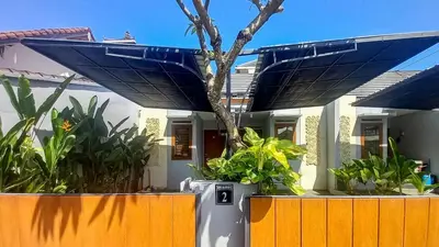 a house with a tree in front of a fence at Andewi Homestay RedPartner - Minimum Stay 30 Nights in Pesanggaran