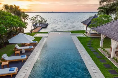 an infinity pool with chairs and umbrellas next to the ocean at Villa Sunset by Premier Hospitality Asia in Nusa Dua
