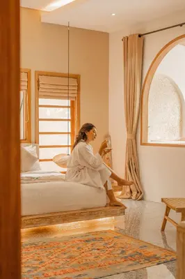 a woman sitting in a bedroom looking out the window at Lamoon Villas Berawa in Canggu