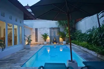 a swimming pool with an umbrella and chairs at Villa Noni Seminyak in Seminyak