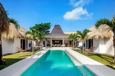 a swimming pool in front of a house with palm trees at Villa Surga Blue by Alfred in Bali in Seminyak