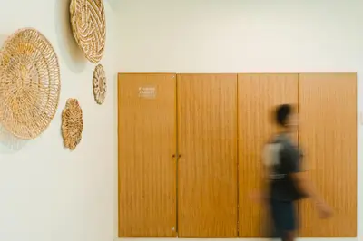 a person walking past a wooden door with hats on a wall at Goestlie Berawa in Canggu