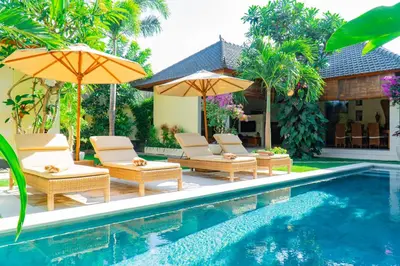 a pool with chairs and umbrellas next to a house at Villa Dayak in Seminyak