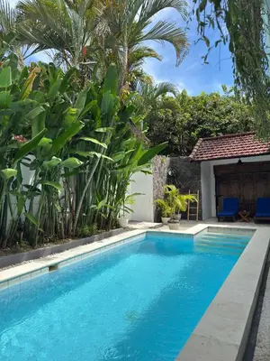 a swimming pool in front of a house with palm trees at Lalita Villas Seminyak in Seminyak