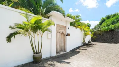 a white house with palm trees in front of it at Villa Aloui by Villa Finder in Kerobokan