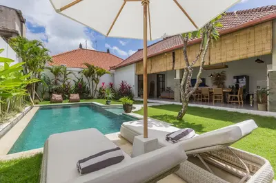 a villa with a swimming pool with chairs and an umbrella at Charming 3 Bedrooms Villa Beach Walking Distance in Seminyak