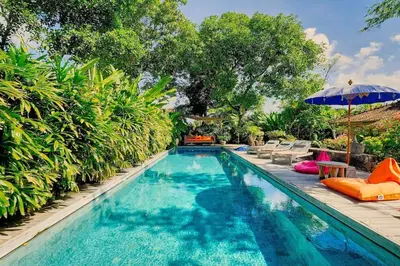 a swimming pool with chairs and an umbrella next to it at Wahyu wonderful private honeymoon joglo in Seminyak