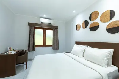 a bedroom with a bed and a desk and a window at Cove Matahari Guesthouse Sunset in Legian