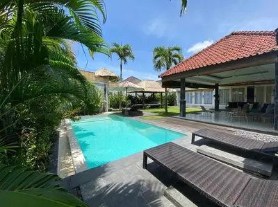 a swimming pool with two benches and a house at Villa Dharsan in Seminyak