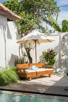 a wooden bench with an umbrella next to a pool at Rumah Ananda Bali - Balinese Villa Umalas in Canggu