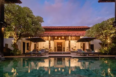 a pool in front of a house with chairs and umbrellas at Villa De Suma - Fully Staffed Luxury Villa, Central Seminyak, walk to the beach in Seminyak