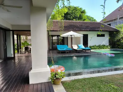 a house with a swimming pool with chairs and an umbrella at Villa Mertasari 10C 4 Bedroom with Swimming pool! in Sanur