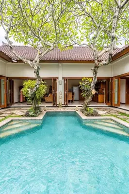 a swimming pool in front of a house with trees at Taman Rahasia by iBali Management in Kerobokan