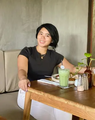a woman sitting at a table with a drink at White Penny Hostel in Seminyak