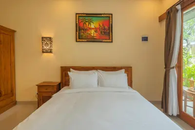 a bedroom with a large white bed and a window at Liliy Guest House Kuta in Legian