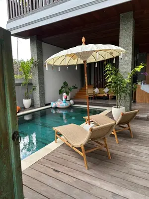 a patio with two chairs and an umbrella next to a pool at Tropical Beach House Bali in Seminyak