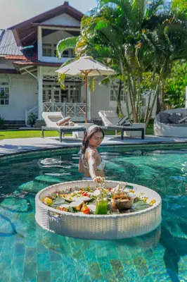 a little girl in a swimming pool with a tray of food at Villa Burung in Kashantee Village in Seminyak