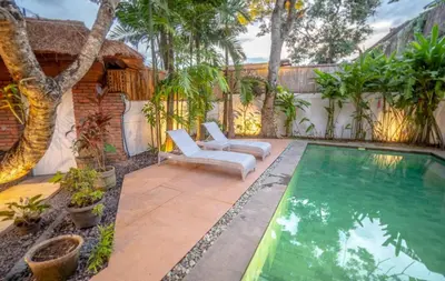 a backyard with a swimming pool and two chairs and trees at Villa Jado 2 - 3 Bedroom Villa With Private Pool in Kerobokan
